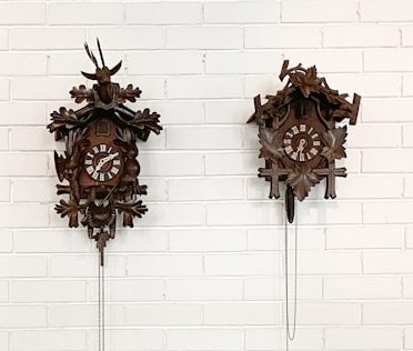 Zwei traditionelle Kuckucksuhren aus Holz an einer weißen Wand.